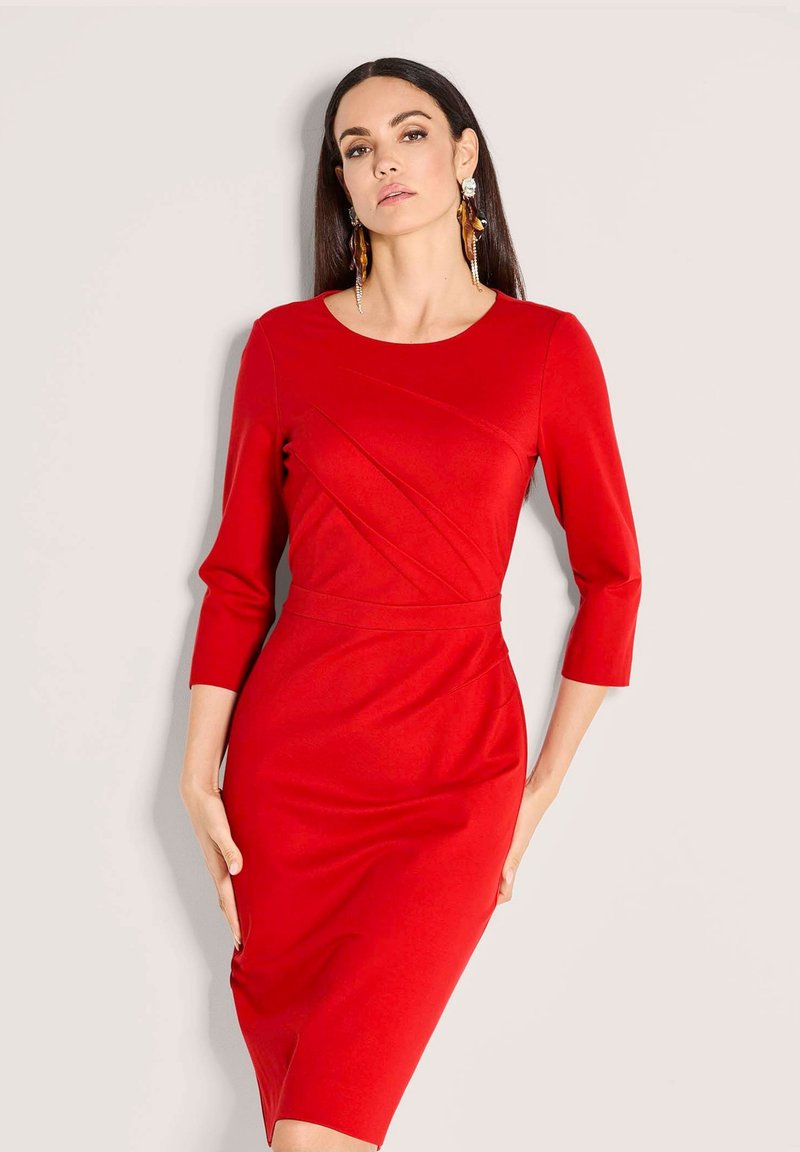 Rotes figurbetontes Kleid mit dreiviertel Ärmeln, rundem Ausschnitt, diagonalen vorderen Nähten und knielangem Saum, aus glattem Stoff gefertigt.
