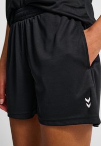 Svarta sportshorts i slät tyg med elastiskt midjeband, med sidofickor och vita logodetaljer.