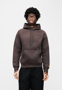 Καφέ φούτερ με κουκούλα, κορδόνι σύσφιξης, μπροστινή τσέπη και ριμπ μανσέτες. Φοριέται με μαύρο παντελόνι cargo. Ομαλή υφή, casual σχεδιασμός.