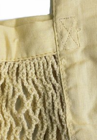 Żółta bawełniana torba tote z plecionką, z gładkim materiałowym wierzchem i przeszyciami. Wykonana z lekkich i elastycznych materiałów.