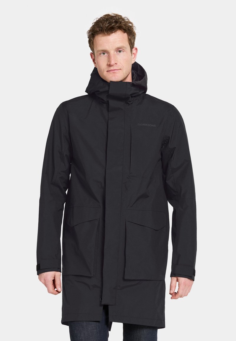 Sorte vandtætte lang jakke med høj krave, justerbar hætte og to store forlommer. Glat, mat tekstur. Minimal branding.