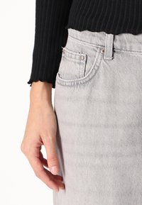 Siva jeans krilo z valovitimi črnim rebrastim puloverjem. Posnetek v bližini roke, ki počiva na žepu, ki vsebuje kovinsko strojno opremo in čiste šive.
