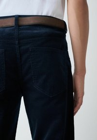 Dark blue corduroy pants with vertical ribbing, featuring two back pockets and a brown leather belt, viewed from the side and back.