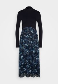 Haut noir à manches longues avec texture côtelée, associé à une jupe imprimée florale bleu marine s'étendant jusqu'au milieu du mollet.