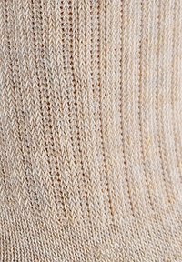 Helles beige gestricktes Socke mit einem gerippten Muster, das vertikale Linien aufweist und aus einem weichen Material gefertigt ist. Keine bemerkenswerten Muster oder Akzente.