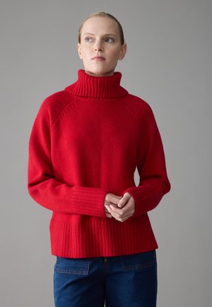 Roter Strickrollkragenpullover mit gerippten Bündchen und Saum, im lockeren Schnitt und mit strukturiertem Stoff. Kombiniert mit blauen Jeans.