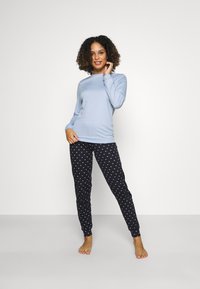 Lichtblauw langer-sleeve top gecombineerd met zwarte joggers met kleine witte hartjespatronen. Zachte stof, aansluitend ontwerp en ribgebreide cuffs.