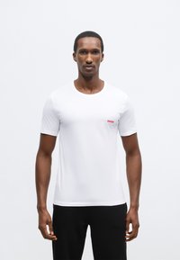 Biele tričko s krátkym rukávom, okrúhlym výstrihom a malým červeným logom "HUGO" na ľavej strane. Hladká tkanina, priliehavý strih.