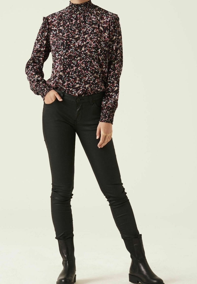 Czarna kwiecista bluzka z długimi rękawami, falbankami na ramionach i wysokim kołnierzem, zestawiona z dopasowanymi czarnymi dżinsami i czarnymi kozakami sięgającymi kolan.