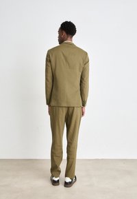 Olive green tailored suit made of textured fabric, featuring a single-breasted jacket with a notched collar and matching trousers.