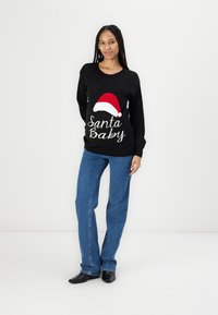 Black sweater featuring a red and white Santa hat design with the text "Santa Baby". Paired with blue denim jeans and black shoes.