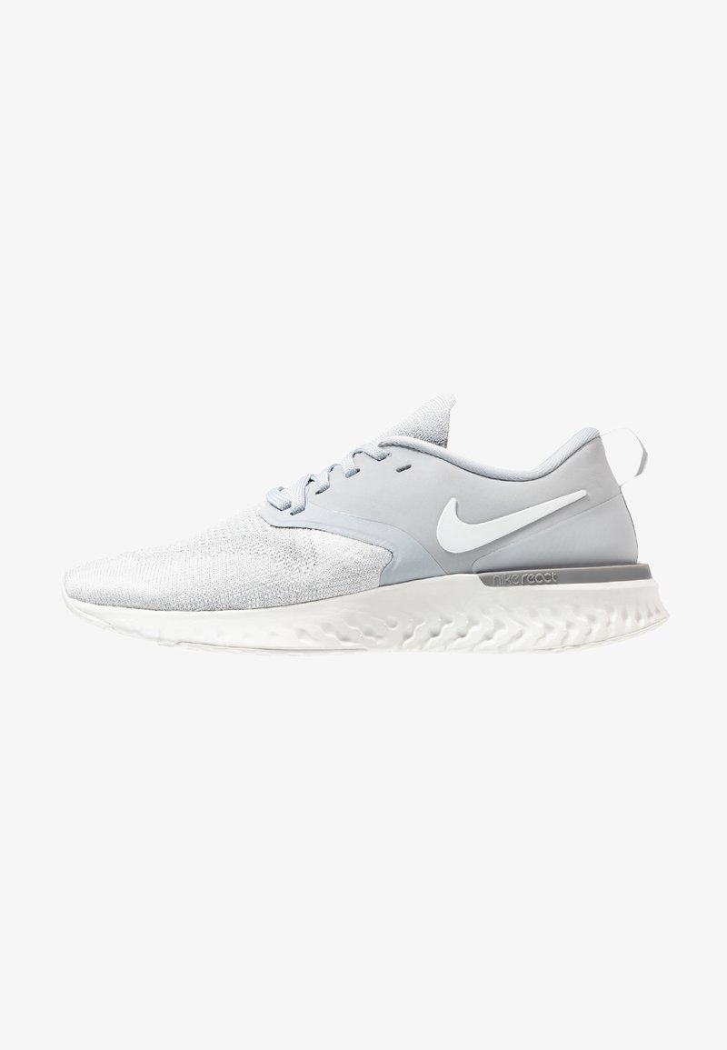 Baskets de sport gris clair avec une tige texturée, des accents lisses et une semelle blanche présentant un motif ondulé. Logo Nike sur le côté.
