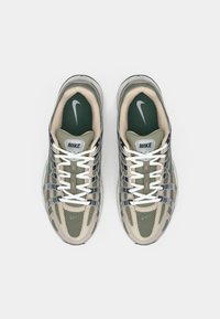 Sneakers Nike z zieloną siateczką u góry, beżowymi akcentami, białymi sznurowadłami i wyściełanym językiem. Posiadają widoczną jednostkę powietrzną w podeszwie.