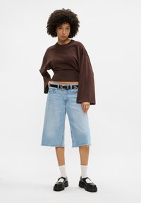 Sweater corto metálico castanho com mangas largas, combinado com culotes de ganga azul claro. Cinto preto com detalhes em prata e sapatos com salto em contraste.