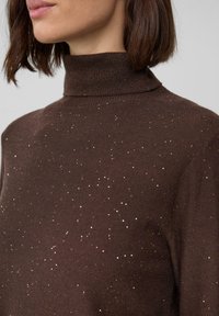 Maglione collo alto marrone realizzato in tessuto knit, con un delicato dettaglio di luccichio sparso sulla superficie. La vista ravvicinata accentua la texture.