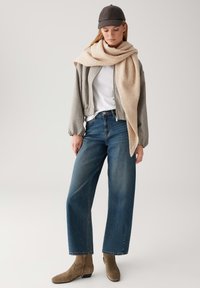 Giacca bomber grigia, maglietta bianca, jeans blu a gamba larga, sciarpa in maglia beige e stivaletti alla caviglia marrone chiaro. Un cappellino completa l'outfit.
