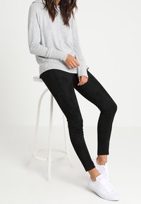 Un haut gris à manches longues associé à des leggings noirs, avec une texture lisse et une coupe ajustée. Complété par des baskets blanches.