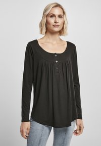 Zwarte lange mouwtop met een ronde hals, knoopsluiting, geplooide voorkant en een zachte, gladde textuur. Draagt samen met lichtblauwe jeans.