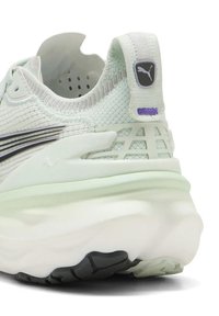 Primo piano del tacco di una sneaker Puma verde chiaro con tessuto a maglia, suola in gomma, linguetta e logo Puma nero.