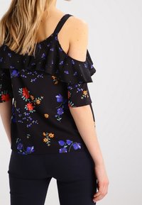 Schwarzes Off-Shoulder-Oberteil mit Rüschensäumen, verziert mit mehrfarbigen Blumenmustern in Rot, Blau und Grün. Glatter Stoff, figurbetonter Schnitt.