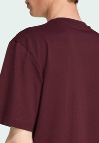 Bordeaux katoenen T-shirt met een klassieke ronde hals, korte mouwen en een zachte textuur, waarbij de achterzijde met minimale stiksels is te zien.