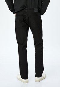 Pantaloni in denim neri con design a gamba dritta, dotati di due tasche posteriori e cuciture sottili. Abbinati a sneaker bianche.