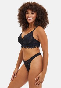 Ensemble de soutien-gorge et string en dentelle noire avec des motifs floraux, des bords festonnés et des sangles réglables. Texture douce et détails de design délicats.