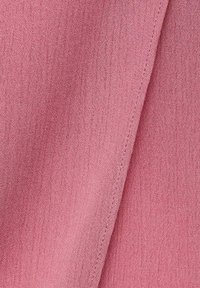 Zachte, gestructureerde stof in een gedempte roze kleur, met een lichte glans en naaddetails langs de rand. Geschikt voor verschillende soorten kleding.