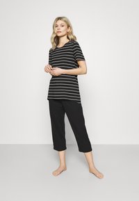 T-shirt a righe bianche e nere con maniche corte, abbinato a pantaloni neri a 3/4. Materiale in cotone; vestibilità rilassata, design semplice.