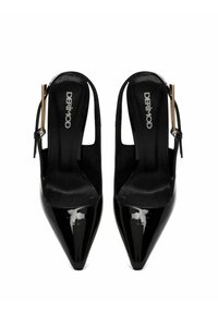 Zapatos de tacón tipo slingback de charol negro con punta afilada, que presentan un diseño recortado y detalles en hardware dorado. Textura suave en toda su superficie.