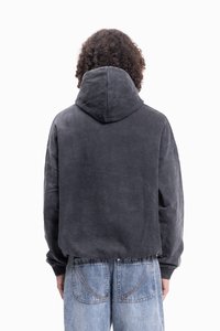 Hanorac cu glugă de culoare gri închis, fabricat dintr-un material moale. Prezintă o croială lejeră și manșete cu dungi. Asortat cu blugi din denim de culoare albastră deschisă.