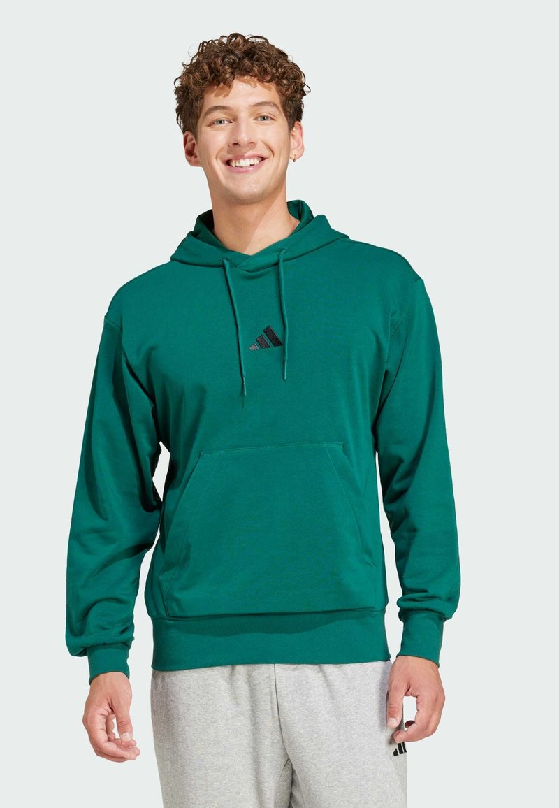Zelená mikina vyrobená z bavlny, s predným vreckom a nastaviteľnou kapucňou so šnúrkou. Obsahuje malé čierne logo na hrudi.