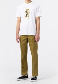 Vit kortärmad t-shirt med ett svart och gult grafiskt tryck. Oljefärgad rakt skuren byxor. Svarta sneakers med vita sulor.