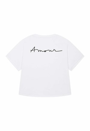 T-shirt blanc avec le mot "Amour" en cursive noire élégante au dos, présentant un design décontracté et stylé.