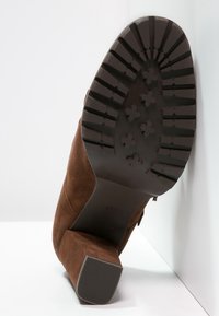 Stivale in suede marrone con punta arrotondata, tacco a blocco di media altezza e suola in gomma decorata con scanalature per la presa.