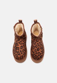 Een paar bruine enkellaarzen met zwart luipaardpatroon en een zachte crèmekleurige voering, gezien van bovenaf tegen een plain witte achtergrond.