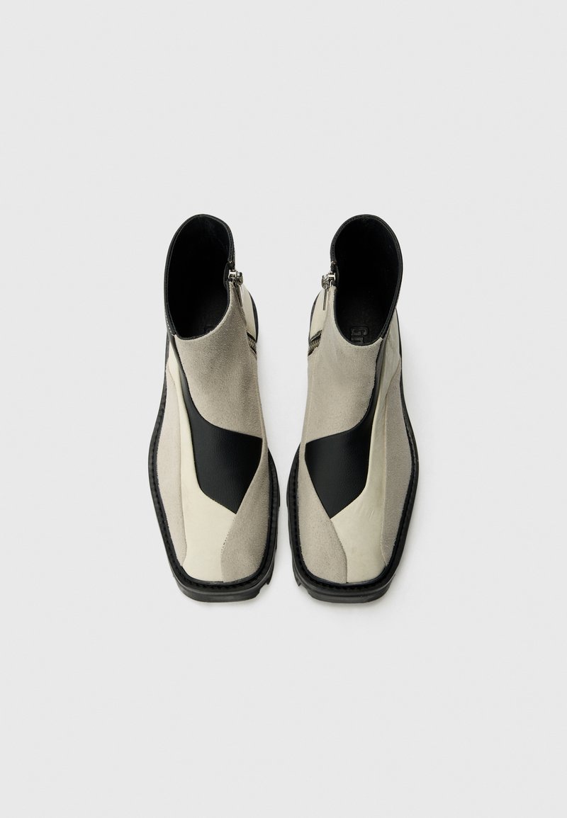 Zwei-farbige Knöchelstiefel mit einem hellgrauen Wildleder-Obermaterial und schwarzen Lederakzenten. Seitliche Reißverschlüsse und eine strukturierte Gummisohle.