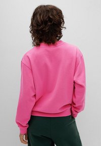 Felpa rosa oversize con collo a giro, polsini e orlo ribattuti; realizzata in tessuto morbido; presenta spalle scese e una consistenza liscia.