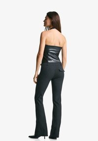 Zwart leren strapless top met een aangesloten ontwerp. Gecombineerd met donkergemarmerde flared broeken. Beide hebben een strakke, gétextureerde afwerking.