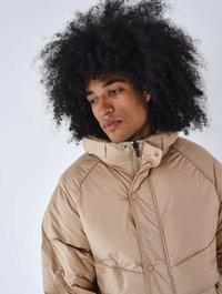 Beige pufferjakke med høj krave, der har en frontlynlås, store knapdetaljer og en quiltet tekstur.