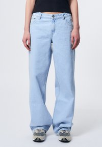 Helle blaue, weit geschnittene Jeans mit klassischem Fünf-Taschen-Design, Knopfverschluss und weichem Denimstoff. Tragen Sie dazu graue Sneakers.