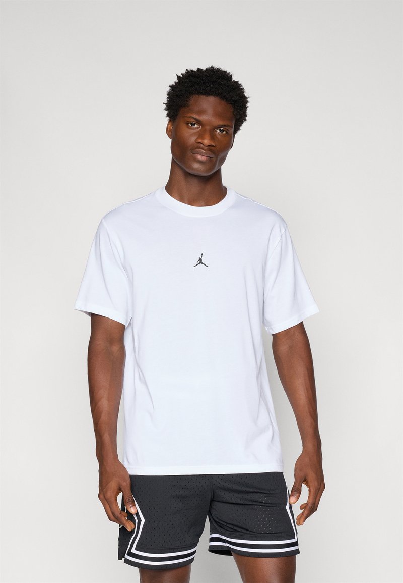 Hvid bomulds t-shirt med korte ærmer, der har et lille sort Jordan-logo på brystet. Bæres med sorte mesh shorts med hvide detaljer.