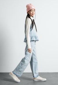 Top peplum de mezclilla azul claro y jeans de tiro alto, combinados con una camiseta blanca de mangas largas y zapatillas beige, rematados con un gorro de punto rosa.