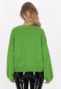 Grön stickad tröja med lös passform, ribbad nederkant och pärlprydnader på ärmarna. Kombineras med svarta, glänsande leggings.