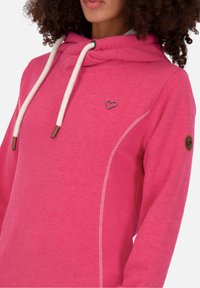 Felpa fucsia con cappuccio e cordino, caratterizzata da cuciture bianche e un logo a forma di cuore sul petto. Tessuto morbido e vestibilità rilassata.