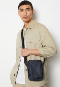 Borsa a tracolla nera in nylon con forma rettangolare, dotata di tasca con zip, cintura regolabile e logo discreto sul davanti.
