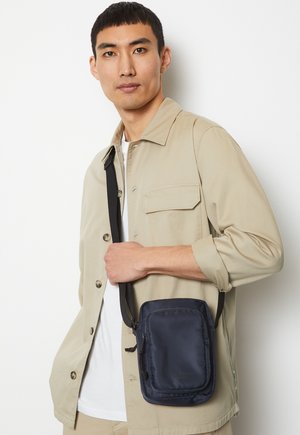 Borsa a tracolla nera in nylon con forma rettangolare, dotata di tasca con zip, cintura regolabile e logo discreto sul davanti.