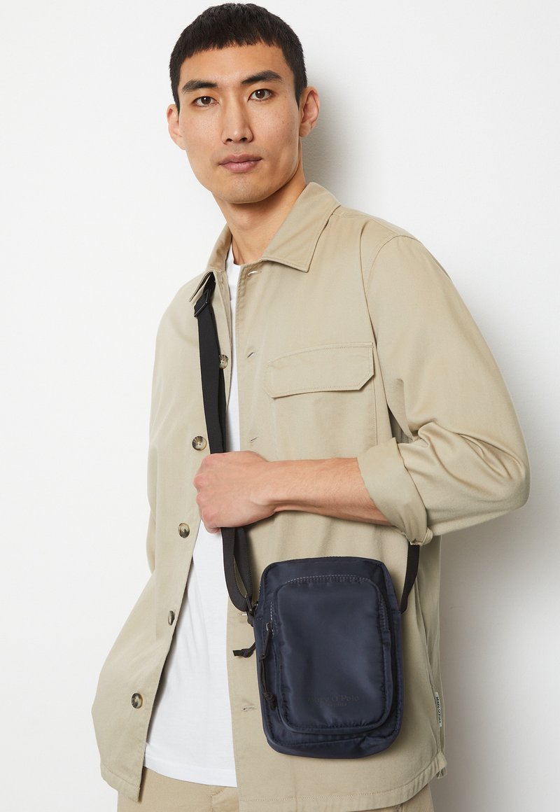 Borsa a tracolla nera in nylon con forma rettangolare, dotata di tasca con zip, cintura regolabile e logo discreto sul davanti.