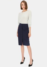 Granatowa spódnica ołówkowa z guzikami z przodu, z dwoma pionowymi kieszeniami. Połączona z jasną, luźną bluzką.