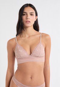 Hellrosa Lace-Bralette mit dreieckiger Form, verstellbaren Trägern und einer gewellten Kante. Zarte Blumenmuster durchgehend.